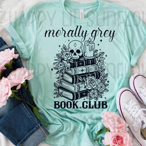 Peut inclure: Un t-shirt vert menthe clair avec une impression graphique noire représentant une pile de livres, un crâne, une bougie et des fleurs. Le texte indique "morally grey" et "BOOK CLUB". Le t-shirt est présenté avec un jean bleu foncé et des baskets blanches.