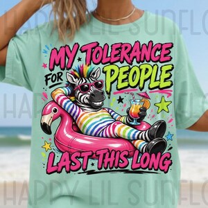 May include: A light green t-shirt featuring a graphic of a zebra wearing rainbow-striped clothing and pink sunglasses, lounging in a pink flamingo pool float while holding a tropical drink. The text reads MY TOLERANCE FOR PEOPLE LAST THIS LONG.