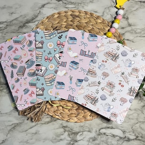 May include: Four rectangular bookmarks featuring repeating patterns of books, coffee cups, flowers, and bows. The designs include a light pink background, a light blue background, a lavender background, and a white background with delicate illustrations.