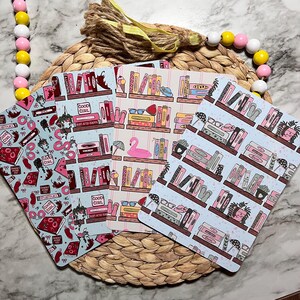 May include: Four rectangular bookmarks featuring colorful illustrations of bookshelves, books, and various small objects like flamingos, plants, and glasses. The designs incorporate shades of pink, red, and blue with text including Good Girl.