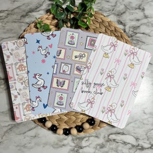 May include: Four rectangular bookmarks featuring various illustrations. One has a stamp pattern with mushrooms, one has geese on blue, one has a stamp pattern with roses and keys, and one has geese on pink stripes with the text silly goose book club.
