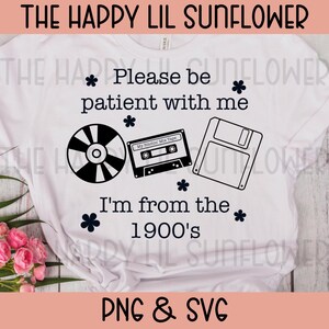 May include: A white t-shirt featuring black text that reads Please be patient with me I'm from the 1900's. The design includes black graphic illustrations of a compact disc, a cassette tape, and a floppy disk, accented by small flower icons.