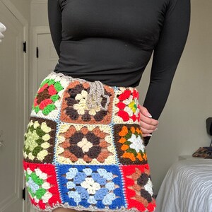 May include: A colorful crochet mini skirt with a patchwork design featuring squares in shades of red, green, blue, brown, yellow, and orange.