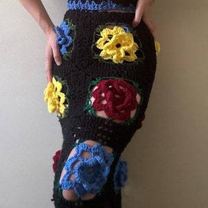 May include: A black crochet skirt with colorful flower appliques. The skirt features red, yellow, blue, and green flowers.