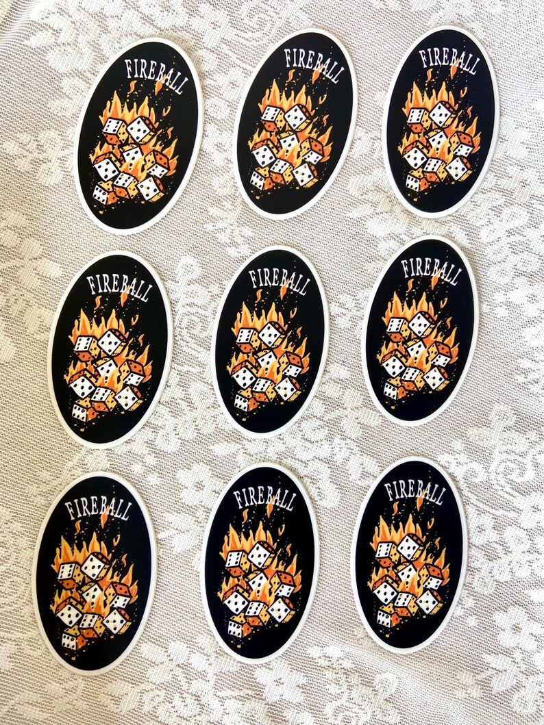 Op de afbeelding: Negen ovale stickers met een zwarte achtergrond en witte dobbelstenen in brand. De tekst "FIREBALL" staat in oranje bovenaan elke sticker.