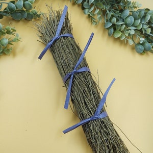 May include: A bundle of dried green branches tied together with purple ribbon. The branches are arranged in a circular shape and are tied with a purple ribbon.
