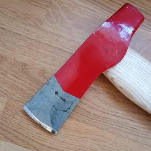 May include: A red and silver axe head with a wooden handle. The axe head is painted red with a silver blade. The wooden handle is light-colored and curved. The axe is designed for chopping wood.