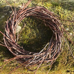 May include: A brown twig wreath, woven into a circle shape, sits on a bed of green moss.