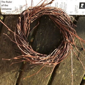 May include: A brown twig wreath, made of thin branches, is arranged in a circle. The wreath is sitting on a wooden surface.
