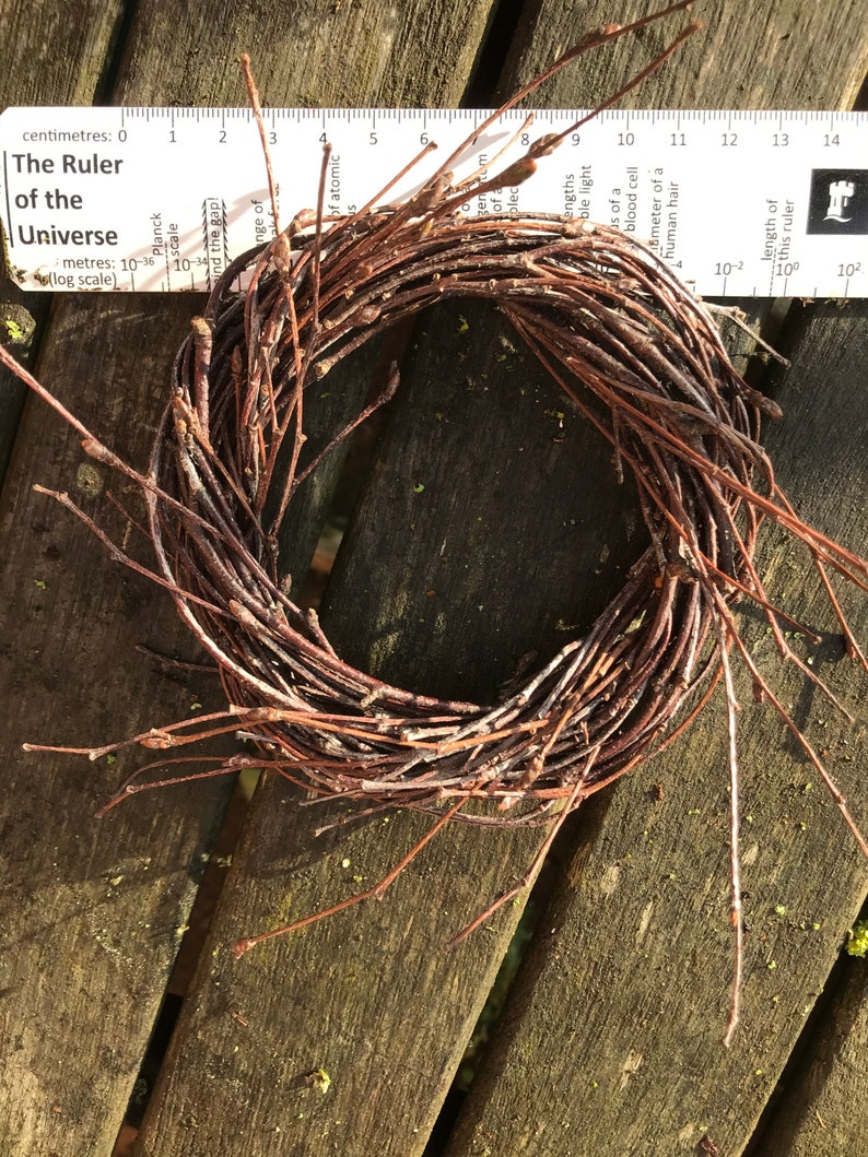 May include: A brown twig wreath, made of thin branches, is arranged in a circle. The wreath is sitting on a wooden surface.