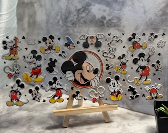 May include: A clear acrylic panel featuring various Mickey Mouse character designs. The panel is supported by a small wooden easel. Mickey Mouse is depicted in various poses, with red, yellow, black, and white colors. The background is a marbled gray.