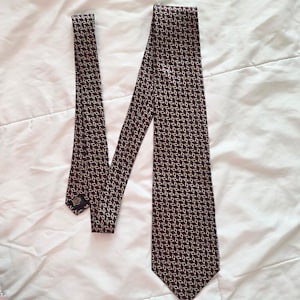 May include: A dark brown tie with a repeating pattern of small, light-colored leaf shapes. The tie is made of a smooth fabric and is displayed on a white surface. The tie is a classic accessory for formal or business attire.