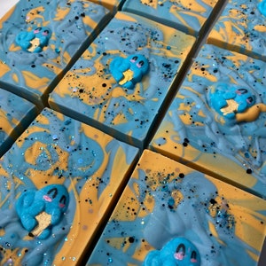 Peut inclure: Plusieurs savons faits à la main avec un motif en spirale bleu et jaune. Chaque savon présente une petite figurine bleue et jaune d'un personnage de dessin animé tenant une étoile.