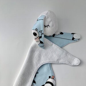 May include: A plush bunny toy with a white head and ears, and a light blue body. The light blue fabric features a repeating panda bear pattern. The bunny has closed eyes and a pink nose.
