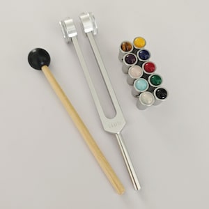 May include: A silver tuning fork with a wooden mallet and a set of 12 colorful gemstone chakra stones. The tuning fork is labeled "128Hz".