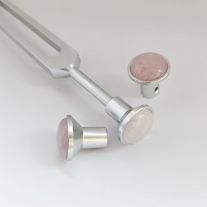 May include: Three silver-toned knobs with pink rose quartz insets. The knobs are round and have a smooth, polished finish.