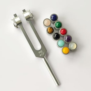 May include: A silver tuning fork with the inscription "RE 417" and a set of 10 colorful gemstone tuning fork strikers.