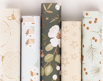 Può includere: Sei rotoli di carta da regalo fantasia. I disegni includono ornamenti dorati, case, fiori bianchi con foglie verdi, stelle dorate e rami di pino con bacche rosse. I rotoli sono disposti verticalmente.