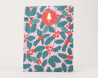 Pode incluir: Um envelope de papel retangular com um padrão repetitivo de folhas de azevinho verde-escuras e bagas vermelhas brilhantes sobre um fundo rosa claro. Um selo adesivo circular vermelho está centrado na aba, exibindo um pinheiro branco e o texto From To.