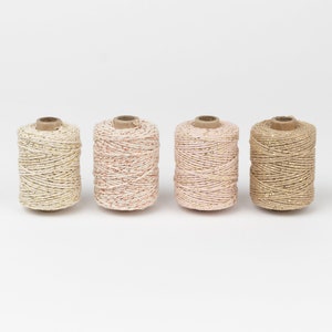Może przedstawiać: Cztery szpulki sznurka z złotym brokatem, w kolorach kości słoniowej, różowego pudru, jasnoróżowego i beżowego.