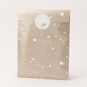 Op de afbeelding: Een ingepakte cadeauzak met een lichtbruine achtergrond en witte stippen. Een gouden kerstboomsticker is in het midden aan de voorkant geplakt. De zak is aan de bovenkant verzegeld.