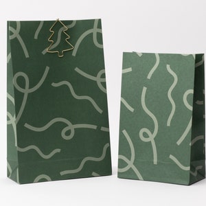 Peut inclure: Deux sacs cadeaux en papier vert avec un motif ondulé gris clair. Le plus grand sac est orné d'un clip en forme de sapin de Noël doré. Les sacs sont de tailles différentes, pour les cadeaux de Noël.