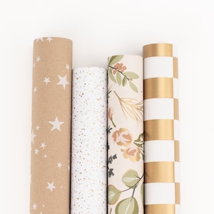 Könnte beinhalten: Vier Geschenkpapierrollen in verschiedenen Designs. Eine Rolle ist Kraftpapier mit weißen Sternen, eine andere ist weiß mit goldenen Sprenkeln, eine dritte hat florale und goldene Akzente, und die letzte hat ein gold-weißes Schachbrettmuster.