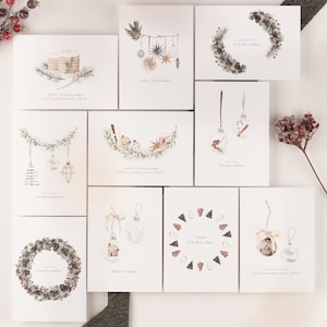 Könnte beinhalten: Eine Sammlung von Weihnachtskarten mit Aquarellillustrationen. Die Karten zeigen festliche Designs wie Ornamente, Kränze und Sterne, mit Text in einer Schreibschrift. Die Farbpalette umfasst Weiß, Grün, Braun und Gold.