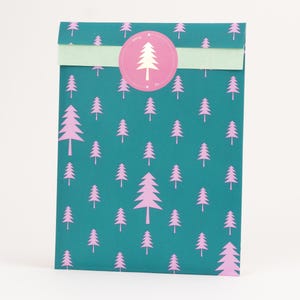 Può includere: Un sacchetto regalo verde acqua con un motivo ripetuto di pini rosa. Una striscia verde chiaro attraversa la parte superiore, con un adesivo circolare rosa con un albero. La borsa è in piedi su uno sfondo bianco.