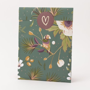 Könnte beinhalten: Ein rechteckiger Papierumschlag mit dunkelgrünem Hintergrund und einem botanischen Muster aus weißen Blüten, orangefarbenen Beeren und einem kleinen Vogel auf einem Zweig. Ein runder, kastanienbrauner Aufkleber mit weißem Herz verschließt die Klappe.