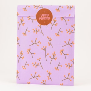 Könnte beinhalten: Eine lila Geschenkverpackung mit einem sich wiederholenden Muster aus braunen Zweigen und orangefarbenen Beeren. Ein runder Aufkleber mit den Worten "Very Merry" in Orange ist auf der gefalteten Oberseite zentriert.