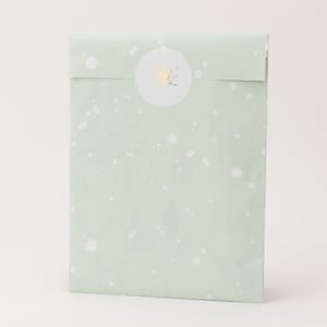 Op de afbeelding: Een lichtgroene cadeauzak met witte spetters en een gouden foliesticker. De sticker heeft een gouden lijntekening van een plant. De zak is aan de bovenkant gevouwen.