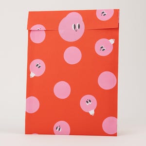 Könnte beinhalten: Ein rechteckiger Papierumschlag in leuchtendem Rot mit einem wiederkehrenden Muster aus hellrosa Kreisen. Einige dieser Kreise sind schlicht, während andere als rosa Weihnachtskugeln mit kleinen Gesichtern und weißen Aufhängern dargestellt sind.