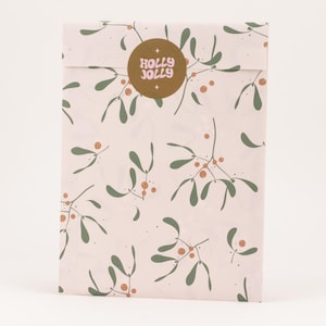 Könnte beinhalten: Ein rechteckiges Paket, verpackt in hellrosa Papier mit einem sich wiederholenden Muster aus grünen Mistelblättern und orangefarbenen Beeren. Ein goldener Aufkleber mit den rosa Worten "HOLLY JOLLY" ist oben angebracht.