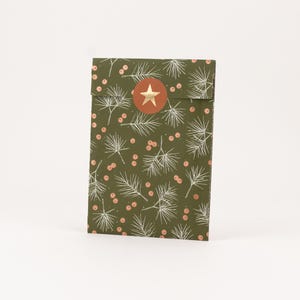 Könnte beinhalten: Eine gefaltete Geschenktüte mit festlichem Design. Die Tasche ist olivgrün mit einem Muster aus weißen Tannennadeln und kleinen rosa Beeren. Ein runder goldener Sternaufkleber verschließt die Klappe.