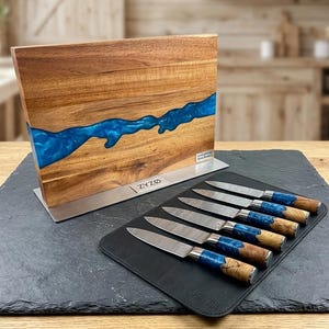 K&ouml;nnte beinhalten: Ein Messerblock aus Holz mit einem blauen Harzfluss-Design, kombiniert mit einem Satz von sechs Messern. Die Messer haben gemusterte Klingen, blaue Harzgriffe und Holzakzente. Der Messerblock und die Messer werden auf einer schwarzen Oberfl&auml;che pr&auml;sentiert.