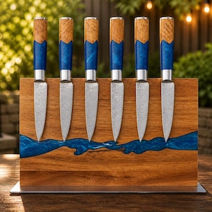 K&ouml;nnte beinhalten: Ein Set aus sechs Steakmessern mit Holzgriffen und blauen Harzakzenten, pr&auml;sentiert in einem Holzblock mit einem blauen Harzfluss-Design. Die Messer haben silberne Klingen und sind vertikal angeordnet.