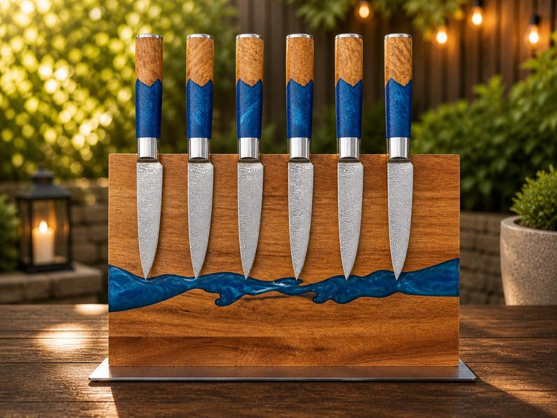 K&ouml;nnte beinhalten: Ein Set aus sechs Steakmessern mit Holzgriffen und blauen Harzakzenten, pr&auml;sentiert in einem Holzblock mit einem blauen Harzfluss-Design. Die Messer haben silberne Klingen und sind vertikal angeordnet.