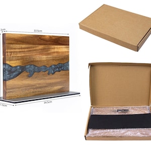 K&ouml;nnte beinhalten: Ein Holzschneidebrett mit einem dunkelblauen Harzfluss-Design. Das Brett ist rechteckig, 33,5 cm lang, 23,5 cm breit und 2 cm dick. Es steht auf einem Metallsockel. Ein Karton ist ebenfalls abgebildet.
