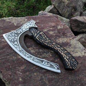 May include: A silver axe with a black wooden handle. The axe head features a decorative design with a compass and other symbols. The handle is carved with a wood grain pattern.
