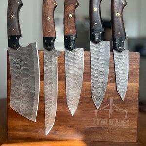 May include: Set of five kitchen knives with wooden handles and Damascus steel blades, displayed on a wooden magnetic knife holder with the text "ZYZO BLADES" engraved on the front.