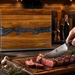 K&ouml;nnte beinhalten: Ein Holzschneidebrett mit einem dunkelgrauen Harzfluss-Design. Ein Steak wird mit einem Messer geschnitten, auf dessen Klinge der Text "ZYZO BLADES" steht. Das Steak liegt auf einem Holzschneidebrett.