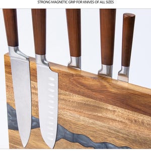 K&ouml;nnte beinhalten: Ein Messerblock aus Holz mit starkem Magnetgriff, der f&uuml;nf Messer h&auml;lt. Die Messer haben Klingen aus Edelstahl und dunkelbraune Holzgriffe. Der Block besteht aus hellbraunem Holz mit einem Flussdesign aus dunkelgrauem Harz. Text: STRONG MAGNETIC GRIP FOR KNIVES OF ALL SIZES.