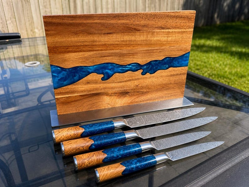 K&ouml;nnte beinhalten: Ein Messerblock aus Holz mit einem blauen Harzfluss-Design, der vier Messer enth&auml;lt. Die Messer haben gemusterte Klingen, blaue und holzfarbene Griffe und einen Edelstahl-Handschutz. Der Block besteht aus Holz und hat einen Edelstahlfu&szlig;.