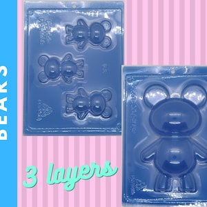 Może przedstawiać: Niebieskie plastikowe formy w kształcie misia do robienia czekoladek lub cukierków. Formy są w dwóch różnych rozmiarach, jedna z trzema małymi misiami, a druga z jednym dużym misiem. Słowo "BEARS" jest wydrukowane pionowo po lewej stronie, a "3 layers" na dole.