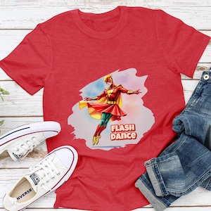 Può includere: Maglietta rossa con una grafica di un supereroe in costume rosso e giallo che balla con il testo "Flash Dance" su uno sfondo di nuvola bianca.