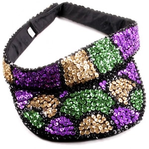 May include: A black visor with a gold, green, and purple sequined design. The sequins are arranged in a geometric pattern.