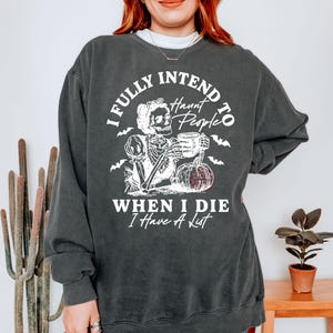 May include: Dark grey sweatshirt featuring a white graphic of a skeleton with a mug and pumpkin. The text says "I FULLY INTEND TO Haunt People WHEN I DIE I Have A List."