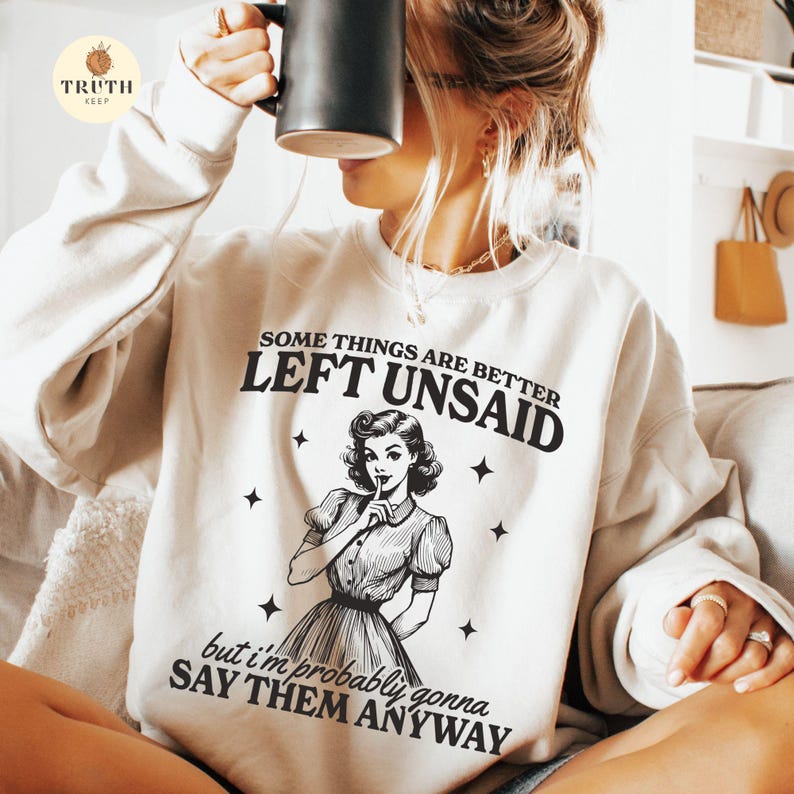 May include: A white sweatshirt with the text "Some things are better left unsaid, but I'm probably gonna say them anyway."  The text is in black and there is a black and white illustration of a woman with her finger to her lips.