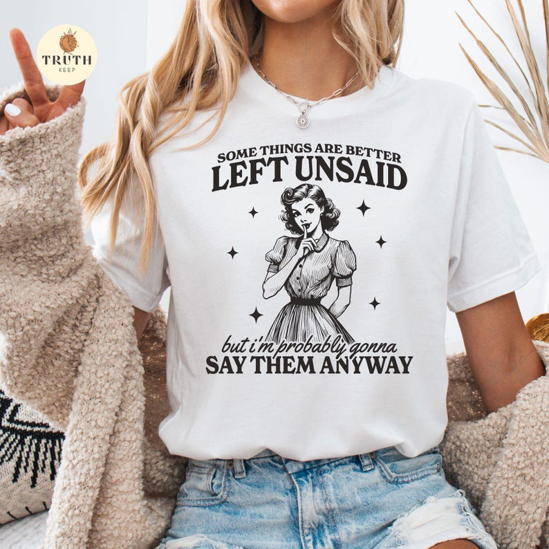May include: White t-shirt with black text that reads "Some things are better left unsaid, but I'm probably gonna say them anyway". A retro-style illustration of a woman with her finger to her lips is above the text.